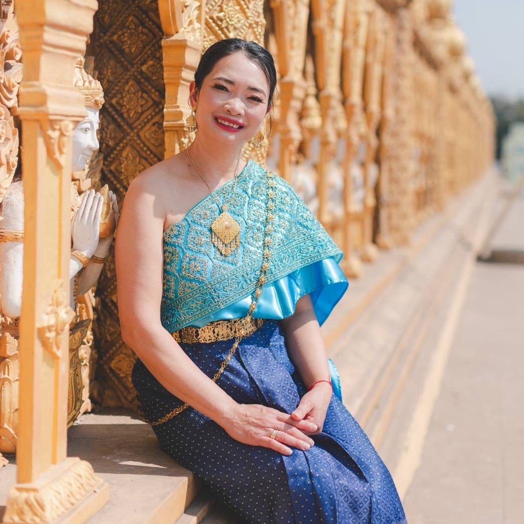 Gung Auf dem Bild ist Gung zu sehen, welche lächelnd vor einem Tempel in Thailand in einem traditionellem thailändischen Gewand sitzt